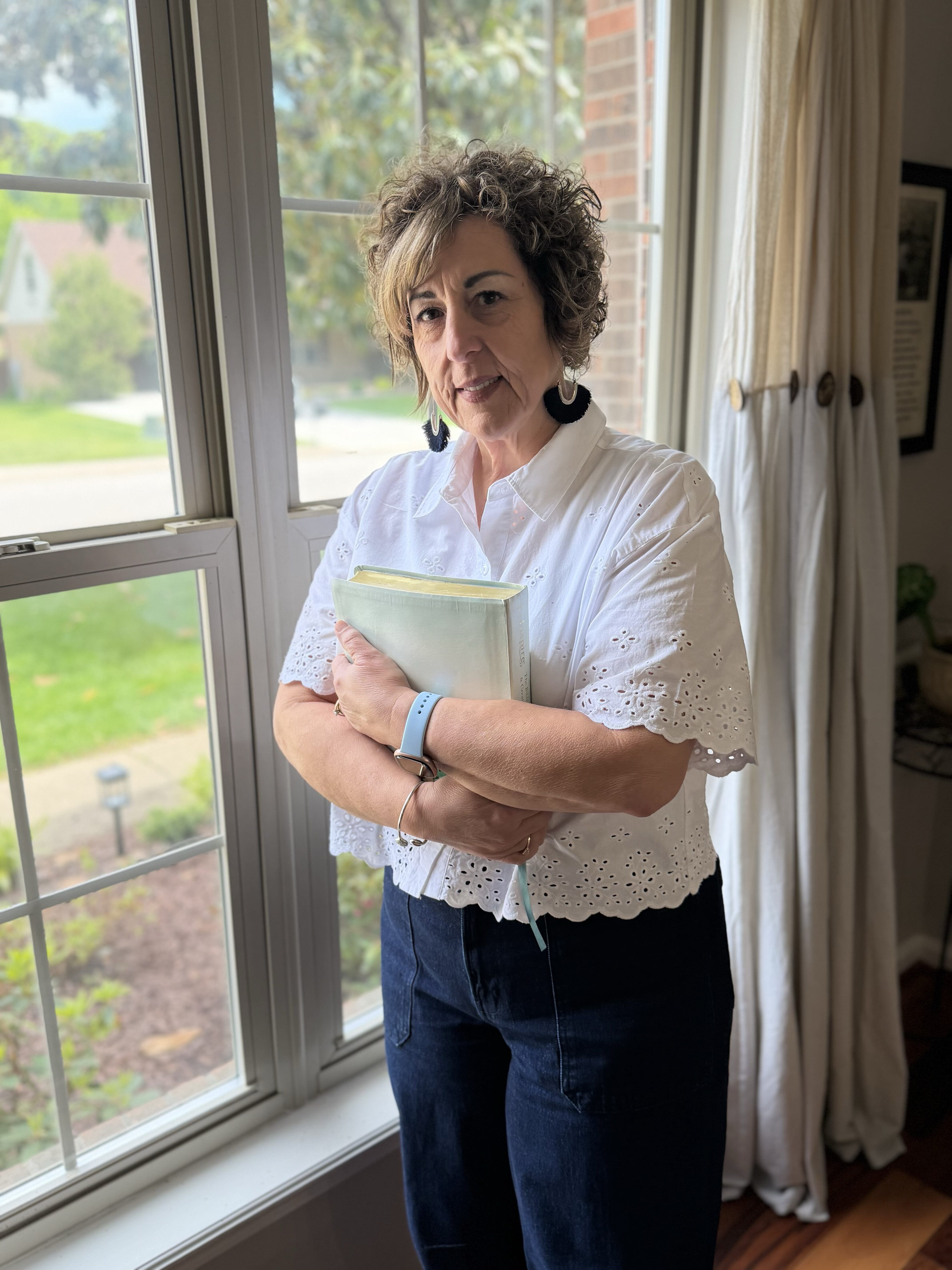 Mother standing quietly by a window in soft natural light, reflecting on loneliness, grief, and God’s presence after child loss.