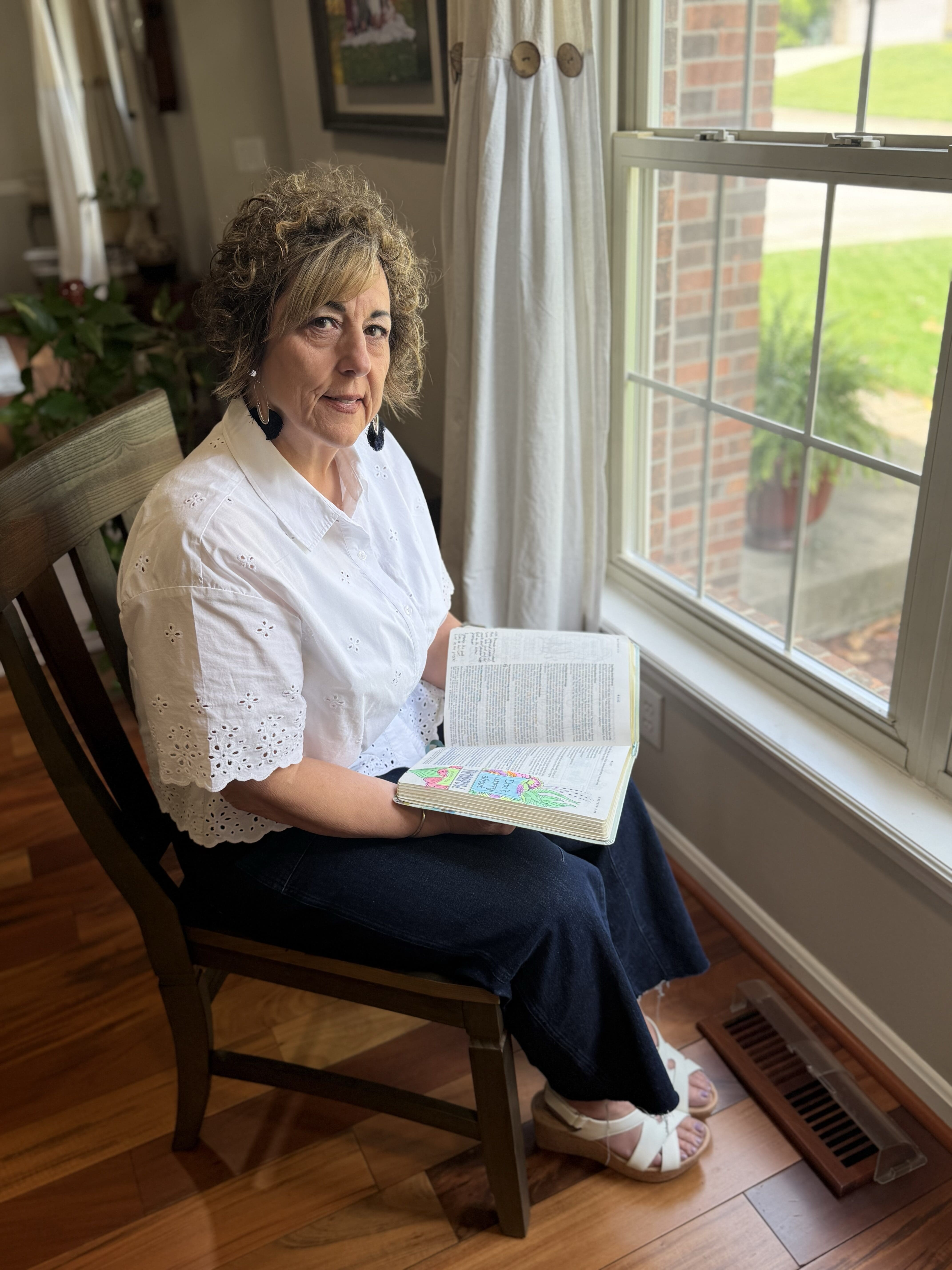 Grieving mother sitting by a window holding her Bible, reflecting on faith, child loss, and learning to trust God with one day at a time.