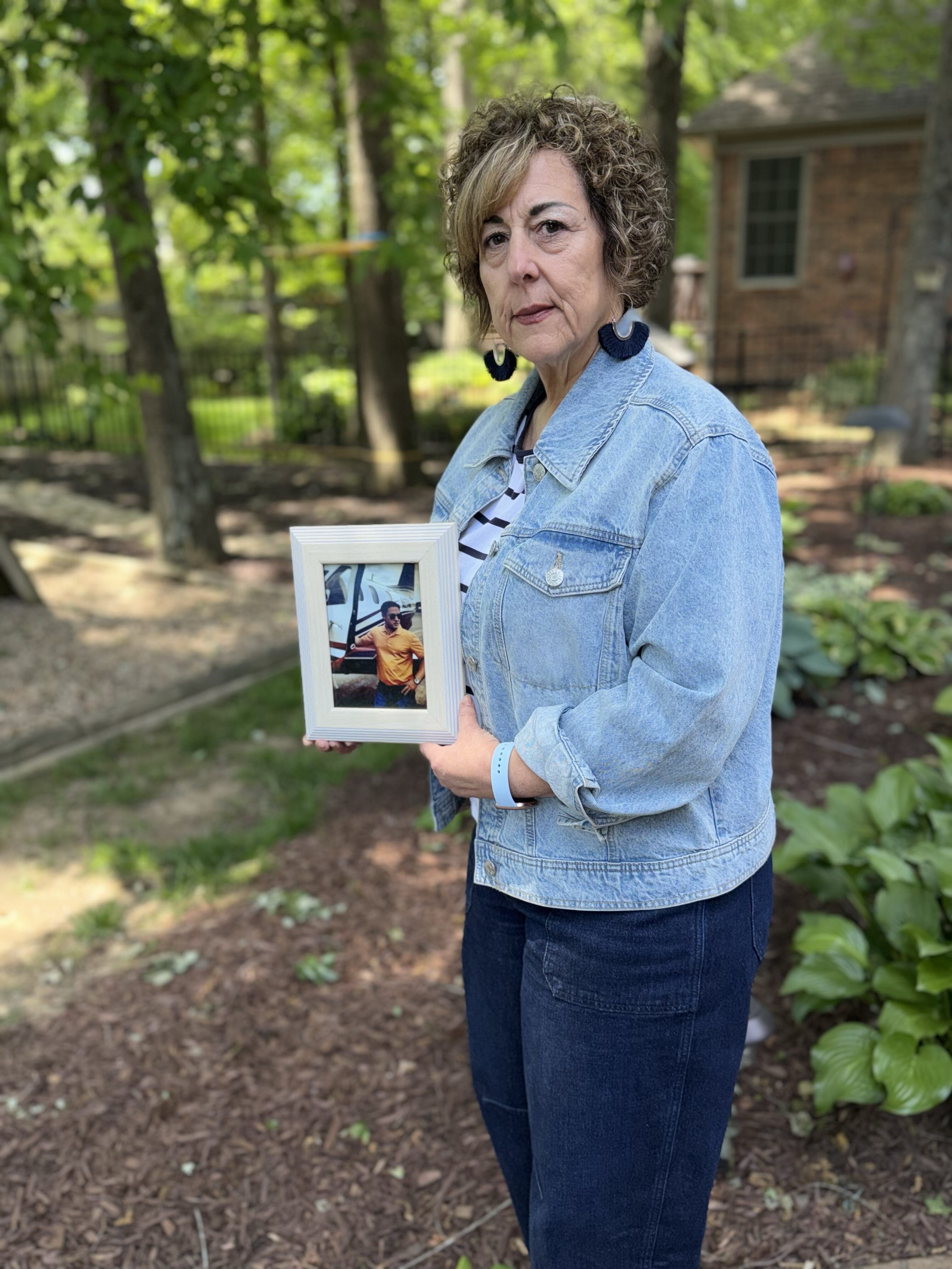 Grieving mother holding a framed photo of her late son, reflecting on carrying his memory with her through every season of life.