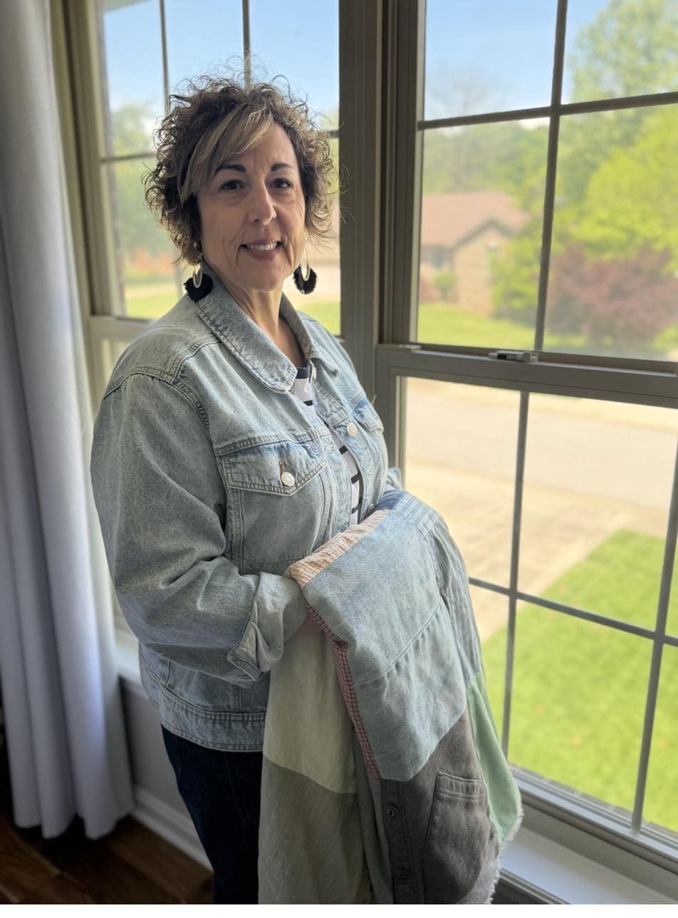 Mother standing in front of a window holding a remembrance blanket after the loss of her child.