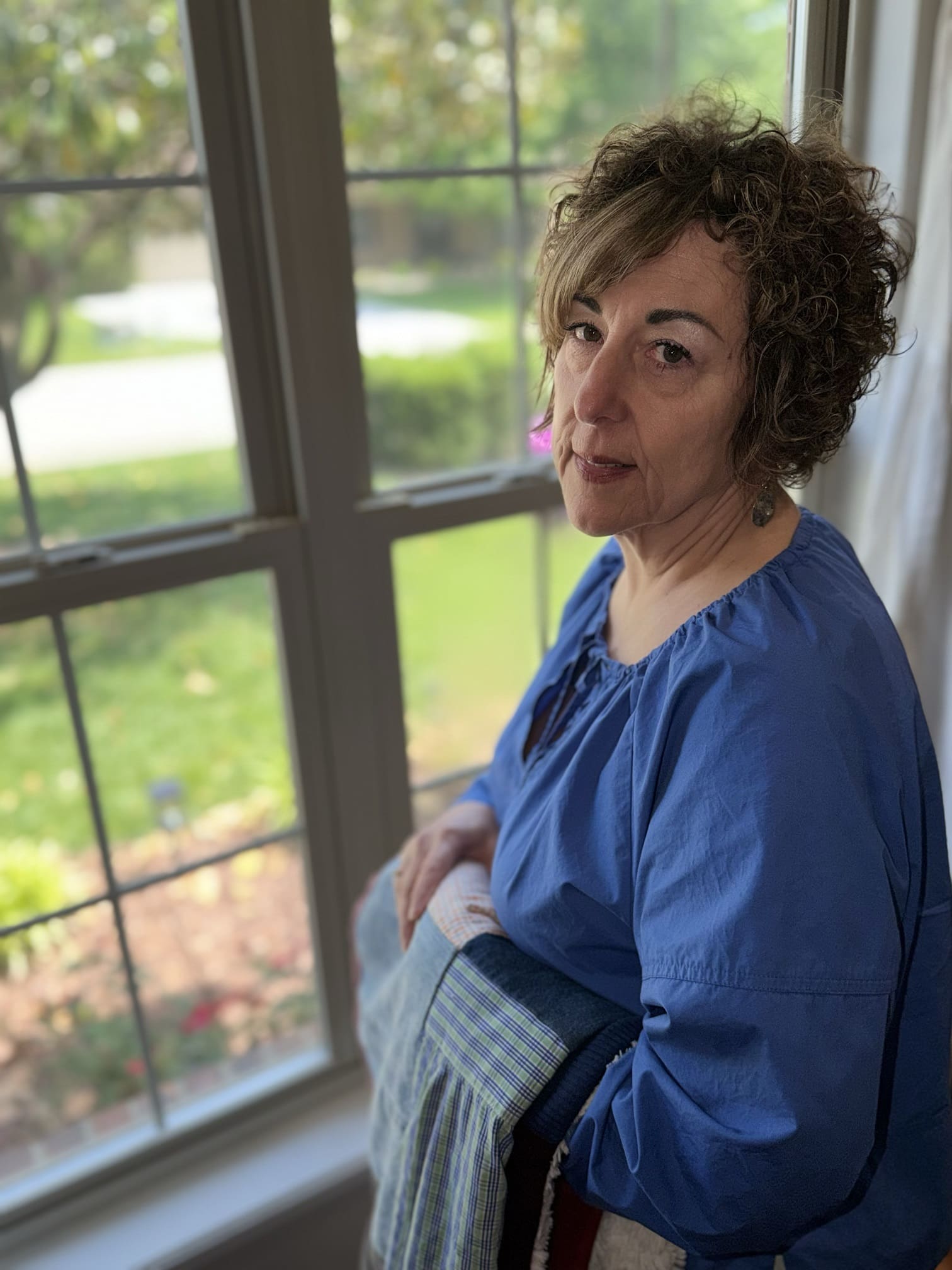 Grieving mother holding remembrance blanket of late son while looking out window